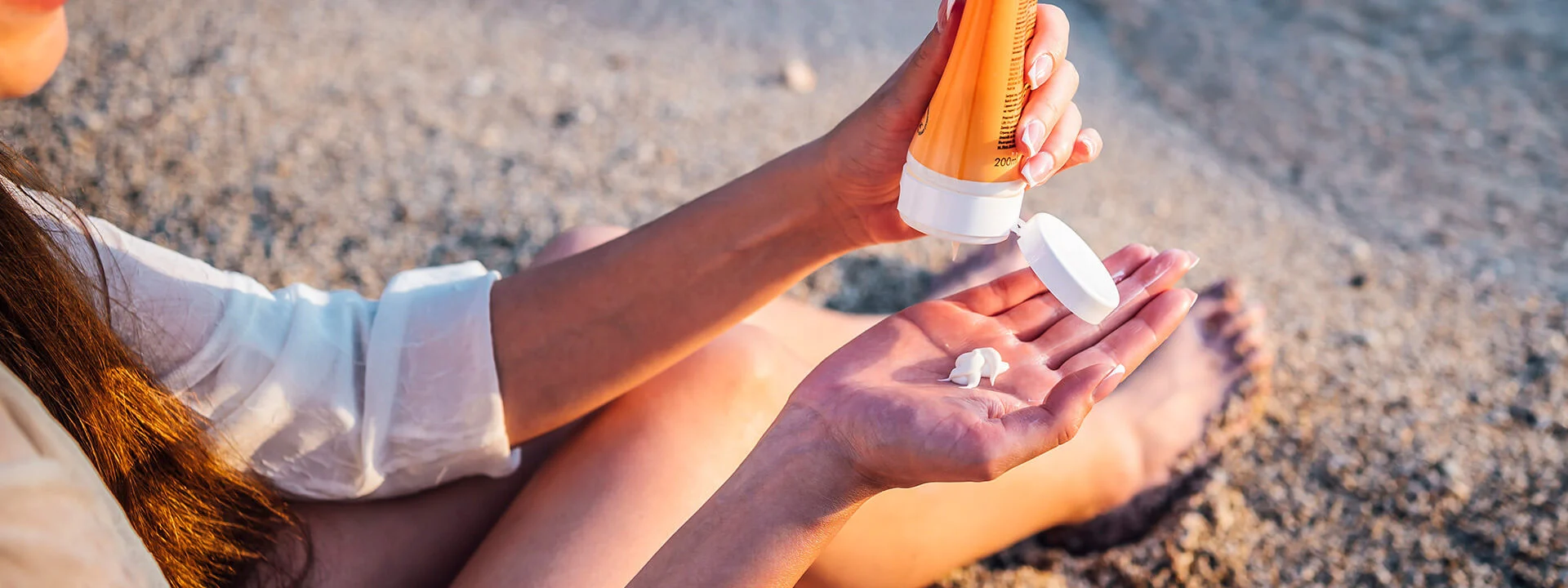 Closeup of someone sitting on beach putting lotion in hand