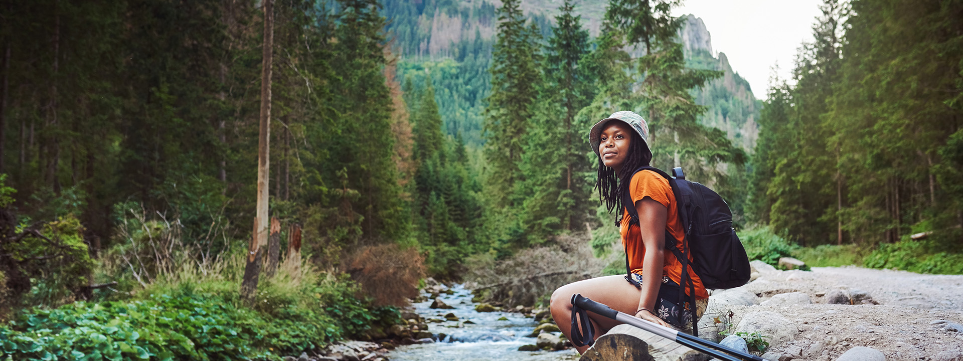 A hiker in the woods, sitting on a log next to a river