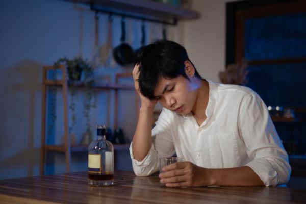 Man sitting in the dark with a glass of liquor. Holding his head in stress.