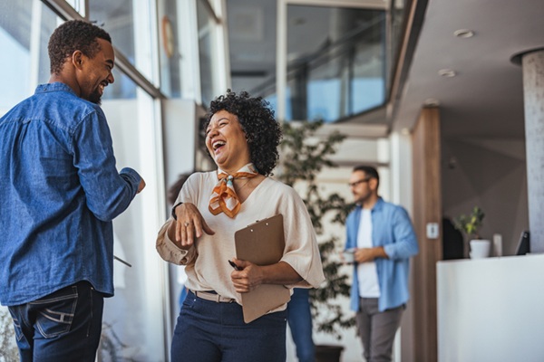 Two coworkers enjoy a lighthearted moment in a bright, modern office environment, conveying teamwork and positivity. The casual atmosphere suggests a collaborative and friendly workplace.