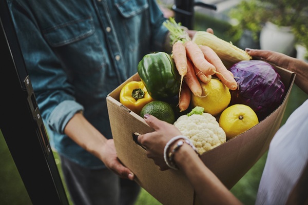 Delivery person handing a box of fresh fruit and vegetables to a customer at the door