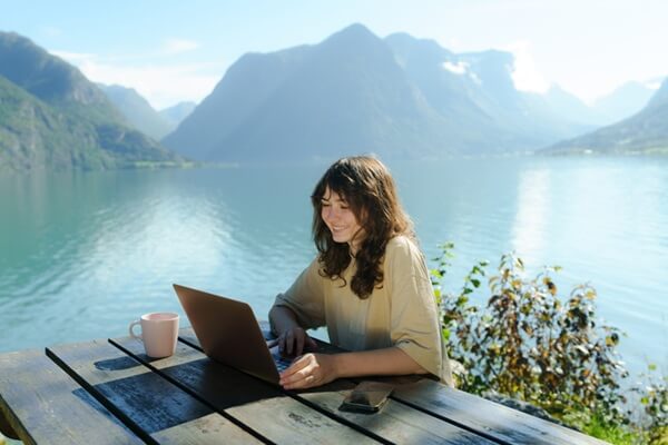 Woman working with laptop and drinking coffee near the pristine lake in Norway