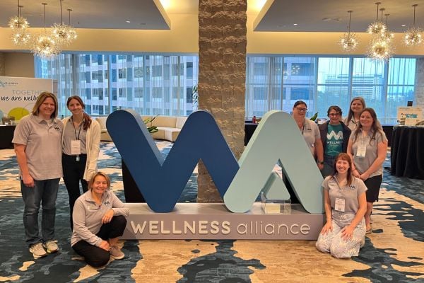 Staff pose next to the Wellness Alliance logo sign
