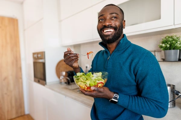 Smiling man stands in the kitchen savoring a home salad bowl
