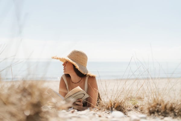 Photo of a young woman enjoying a day at the beach and reading a book