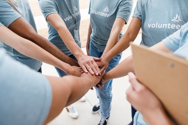 Teamwork, unity, and collaboration shown by diverse group of volunteers stacking hands.