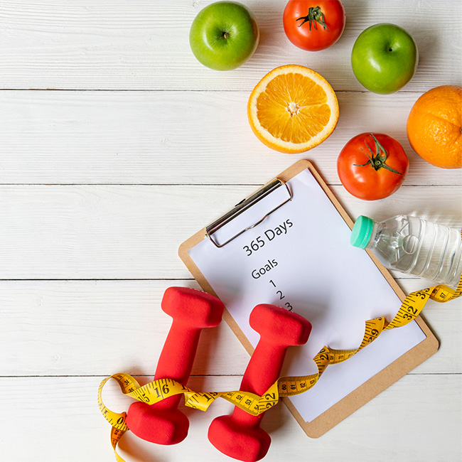A clipboard holding a 365 day goal list, surrounded by healthy food and exercise items