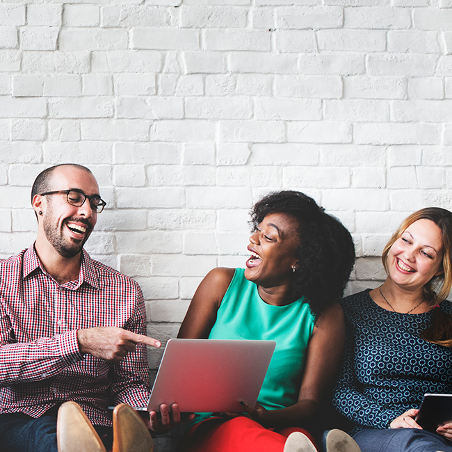 Group of people sitting against a wall with a laptop, smiling and laughing