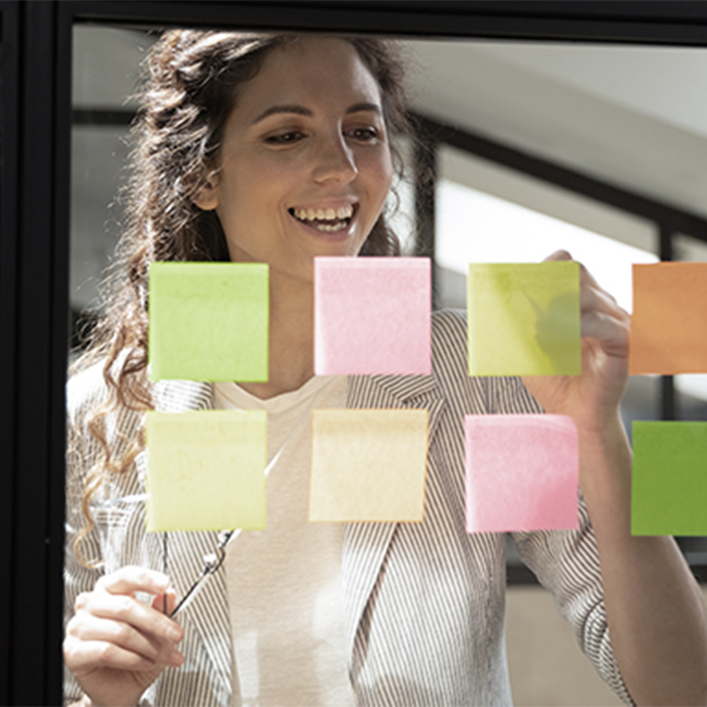 A smiling woman writing on sticky notes stuck on glass