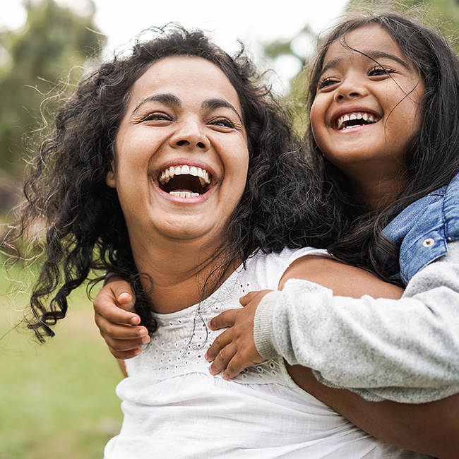 A woman carrying a girl on her back, both smiling