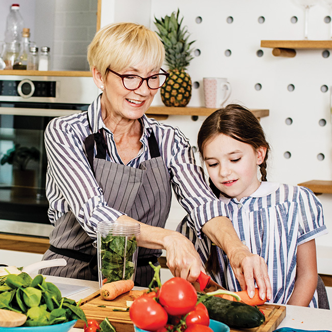 An older woman showing a young girl how to cut vegetables