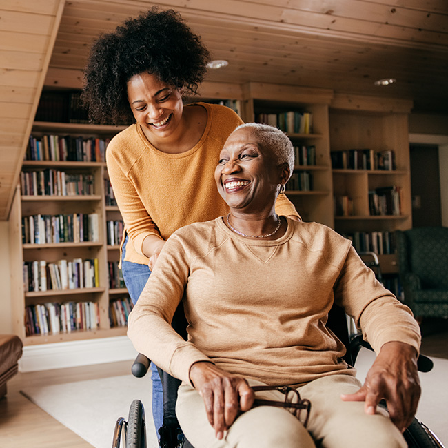 Two women smiling, one pushing the other in a wheelchair
