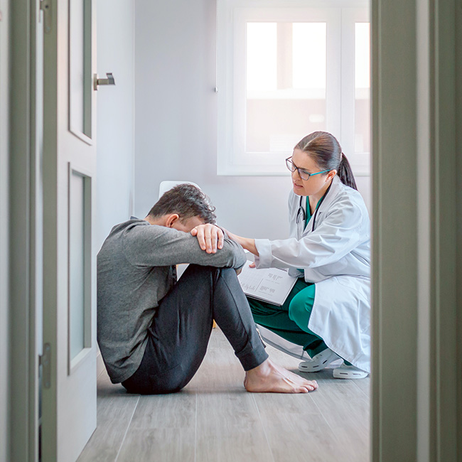A man sitting on the floor with head down, and a health professional consoling him