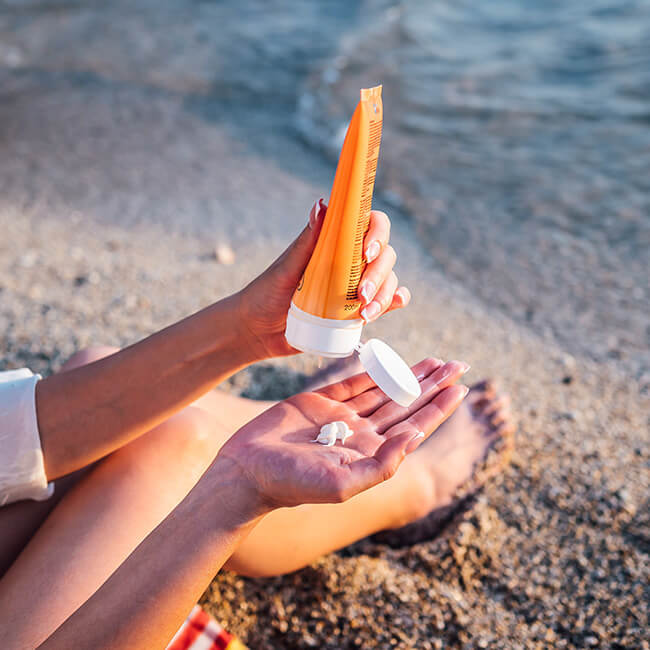 Closeup of someone sitting on beach putting lotion in hand