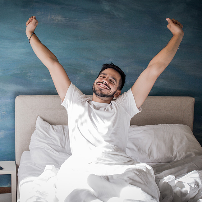 Smiling man waking up in bed and stretching